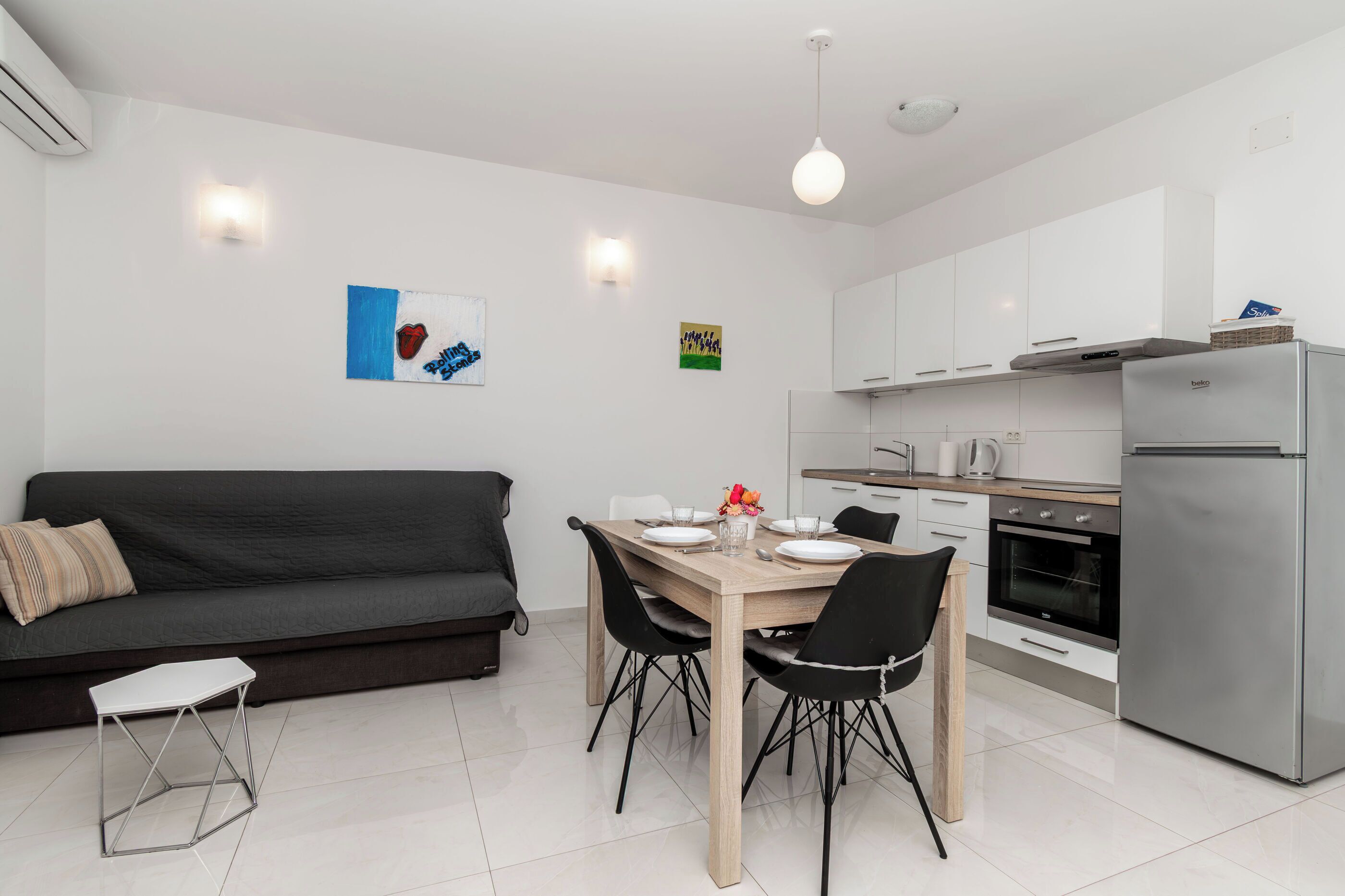 A modern kitchen with white cabinets, a stainless steel refrigerator, and a dining area with a wooden table and black chairs.