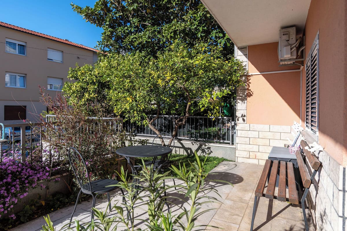 A balcony with a table and chairs, surrounded by plants and a tree.