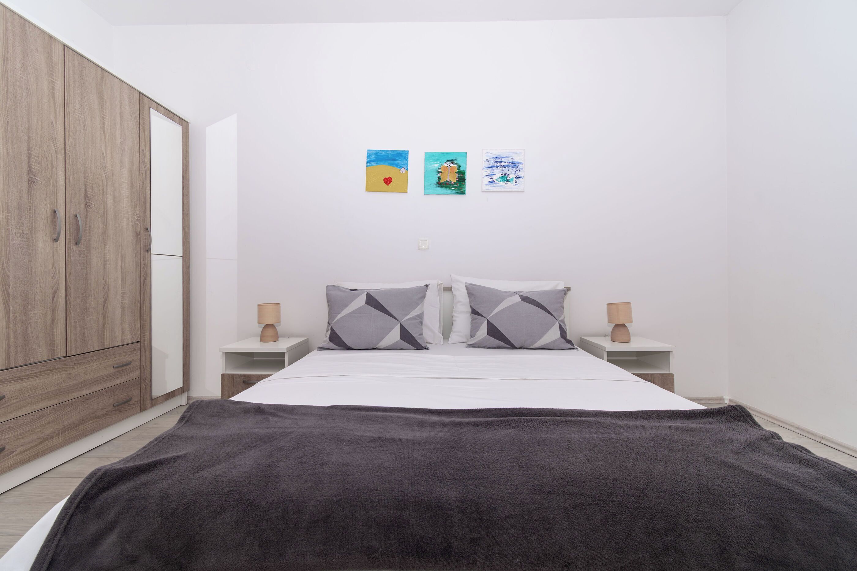 A bedroom with a bed, nightstands, a wardrobe, and wall art.