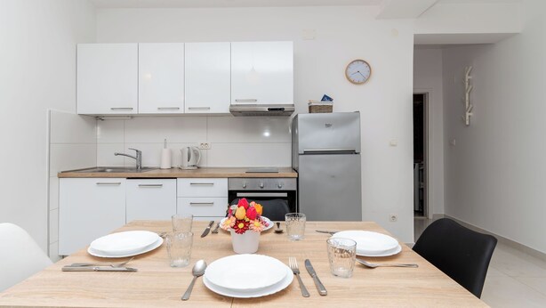Une cuisine moderne avec des meubles blancs, une table à manger en bois et une horloge au mur.