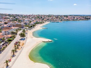 Eine Küstenstadt mit Sandstrand, klarem, blauem Wasser und Wohnhäusern entlang der Uferlinie.