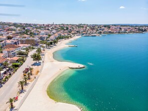 Un pueblo costero con una playa arenosa, aguas azul turquesa y edificios residenciales a lo largo de la costa.