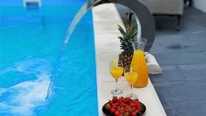 A swimming pool with a water feature, a pineapple, a glass of orange juice, and a bowl of strawberries. - House D&D (Okrug)