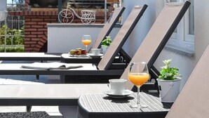 A sunlit outdoor seating area with lounge chairs, a table with a drink, and a decorative metal bicycle. - House D&D (Okrug)