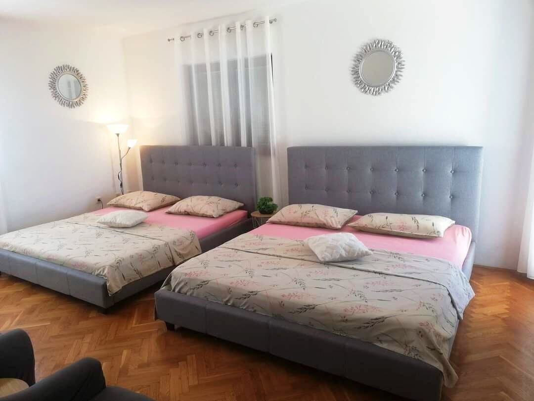 Ein Doppelzimmer mit zwei Betten, jeweils mit grau gepolsterten Kopfteilen und floralem Bettbezug.