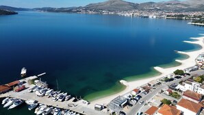 A marina with boats docked, a sandy beach, and a town in the background. - House D&D (Okrug)
