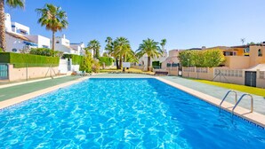 Une piscine à l’eau d’un bleu cristallin, entourée de palmiers et de bâtiments aux façades blanches et beiges.