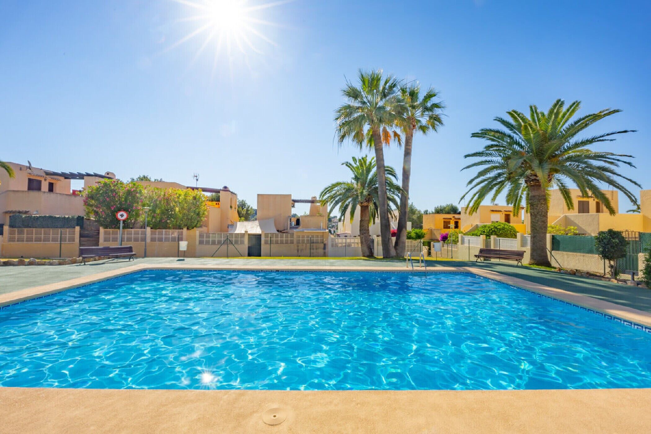 Ein Swimmingpool mit klarem, blauem Wasser, umgeben von Palmen und Gebäuden im mediterranen Stil.