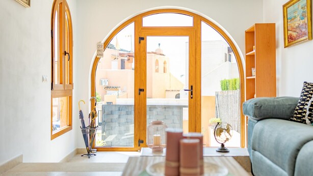 Un salon avec vue sur un immeuble, visible à travers un grand portail en arc de cercle. On y trouve un canapé et une petite table sur laquelle sont posés des bougies et un globe terrestre.