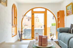 A living room with a view of a building through a large arched doorway. There is a sofa and a small table with candles and a globe. - Welcome Bungalow - PlusHolidays (Calpe)