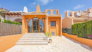 Un bâtiment dont l’entrée est pavée de pierres, avec un petit jardin et un ciel d’un bleu éclatant.