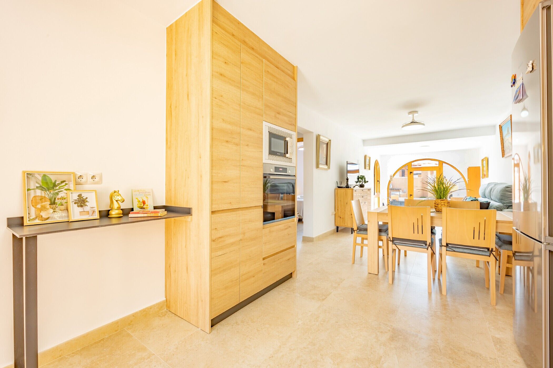 A modern kitchen with wooden cabinetry, a dining area with a wooden table and chairs, and a built-in oven.