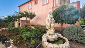 A garden with a statue, potted plants, and a building in the background. - Apartment Massimo Brooklyn (Tribunj)