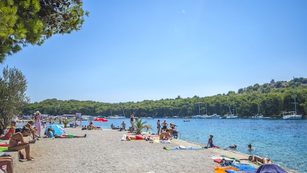 A beach with people sunbathing and swimming, boats in the water, and a forested hill in the background. - Apartment Massimo Brooklyn (Tribunj)