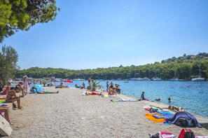 A beach with people sunbathing and swimming, boats in the water, and a forested hill in the background. - Apartment Massimo Brooklyn (Tribunj)