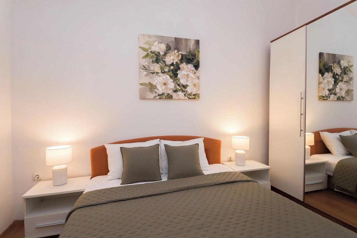 Een hotelkamer met een bed, nachtkastjes, een spiegel en twee schilderijen aan de muur.
