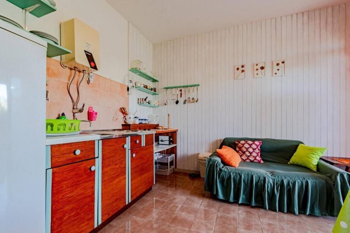 Une cuisine compacte avec des meubles en bois, un évier et un plan de travail. On y trouve un canapé vert avec des coussins et une petite table avec une lampe.