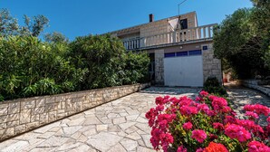 Ein modernes, zweistöckiges Gebäude mit Natursteinfassade, Garage und einem angelegten Garten mit rosa Blüten.