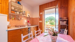 Eine gemütliche Küche mit Holzausstattung, einem Esstisch mit rosa Tischdecke und einem Fenster mit Blick auf einen Garten.