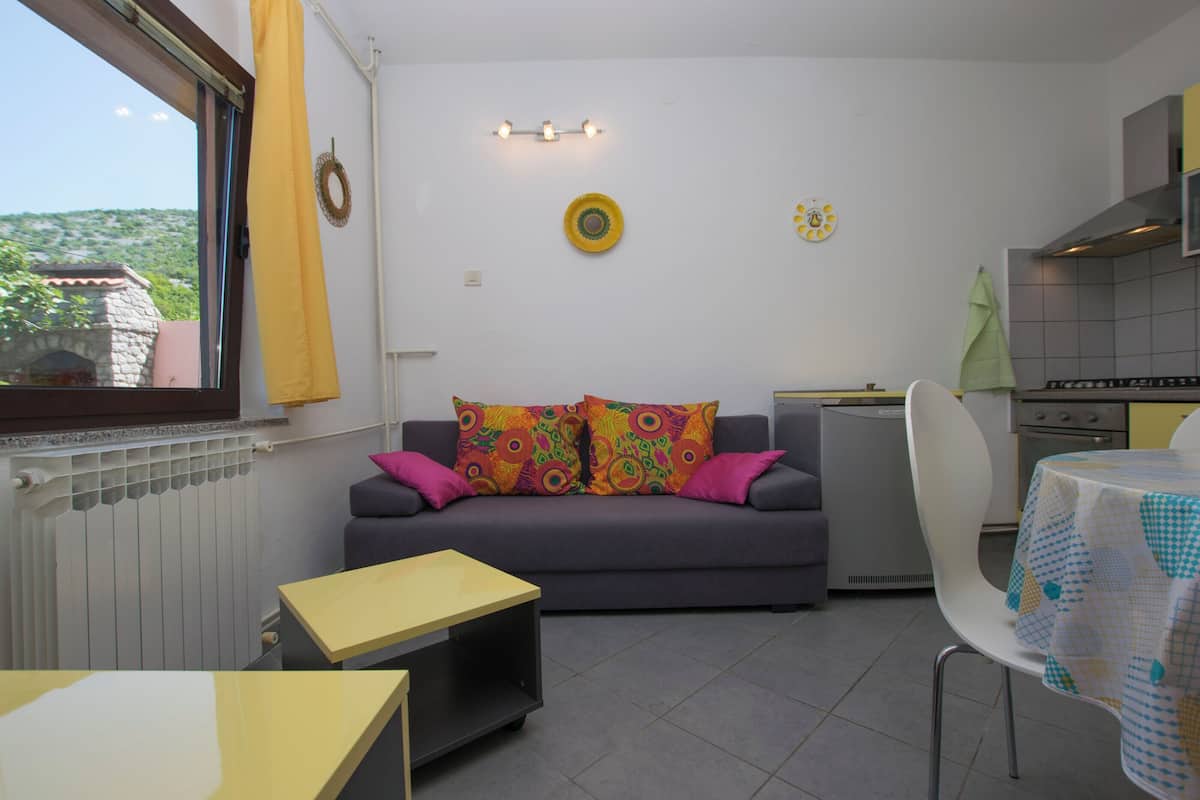 A compact living space with a sofa, a small table, a dining table, and a kitchen area.