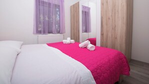 Een slaapkamer met een bed, een grote spiegel en een raam met paarse gordijnen.