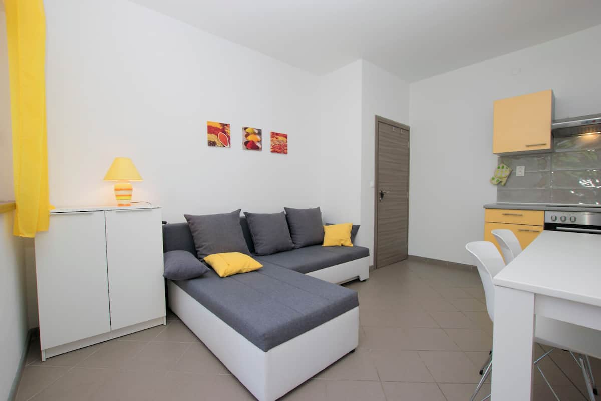 A modern living room with a sofa, a dining table, and a kitchen area.