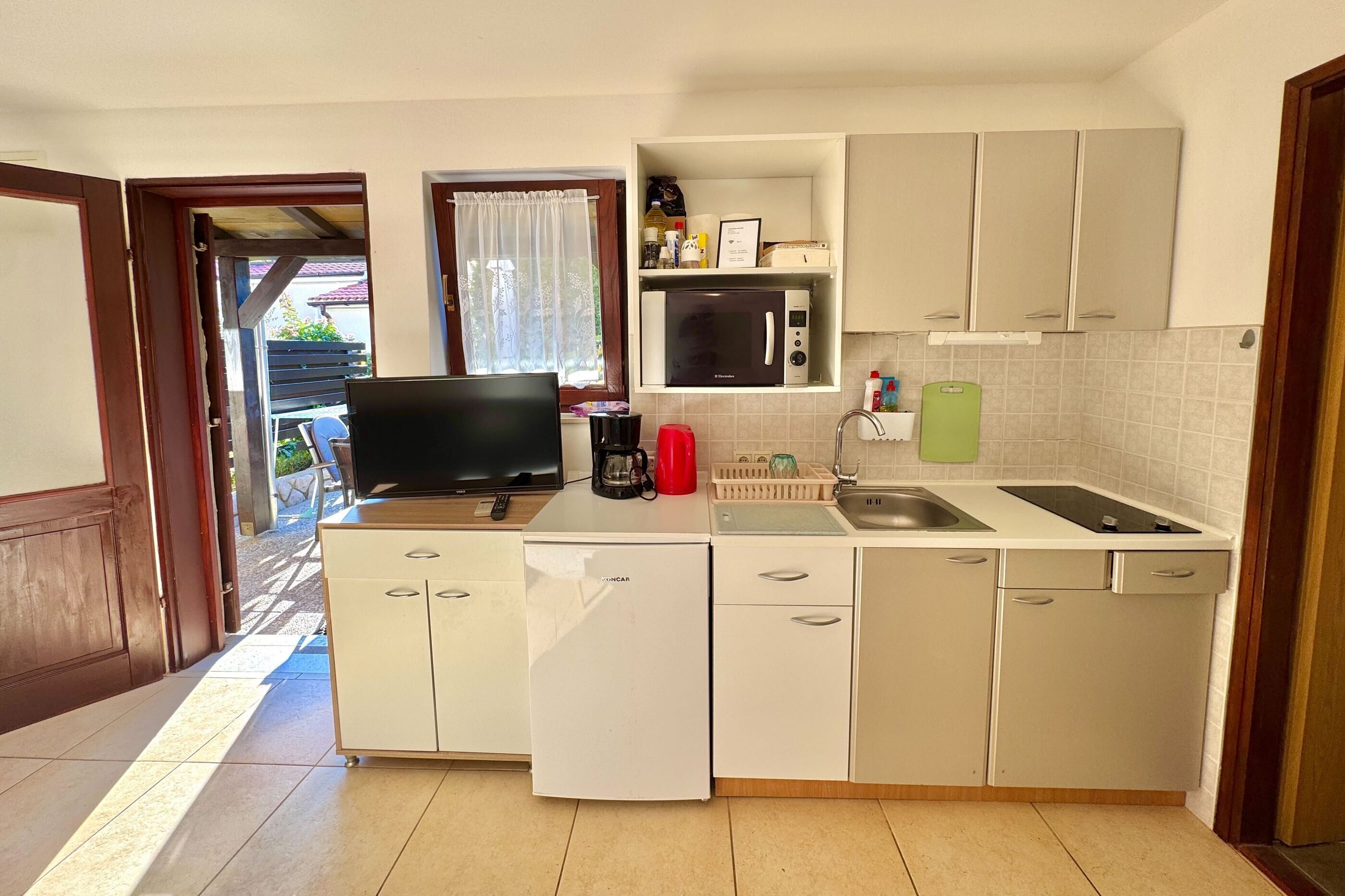 A compact kitchen with white cabinets, a microwave, a sink, and a television.