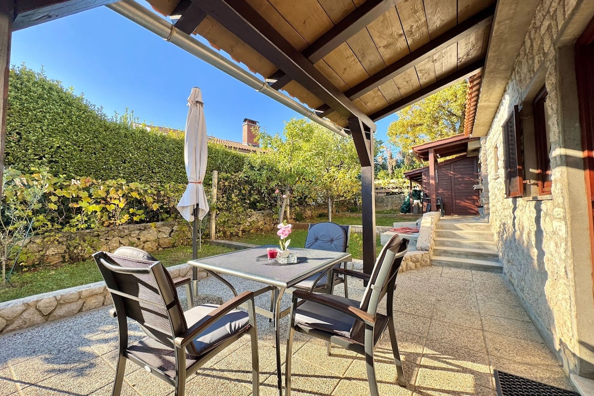 An outdoor patio with a table and chairs, a covered area, and a stone wall.