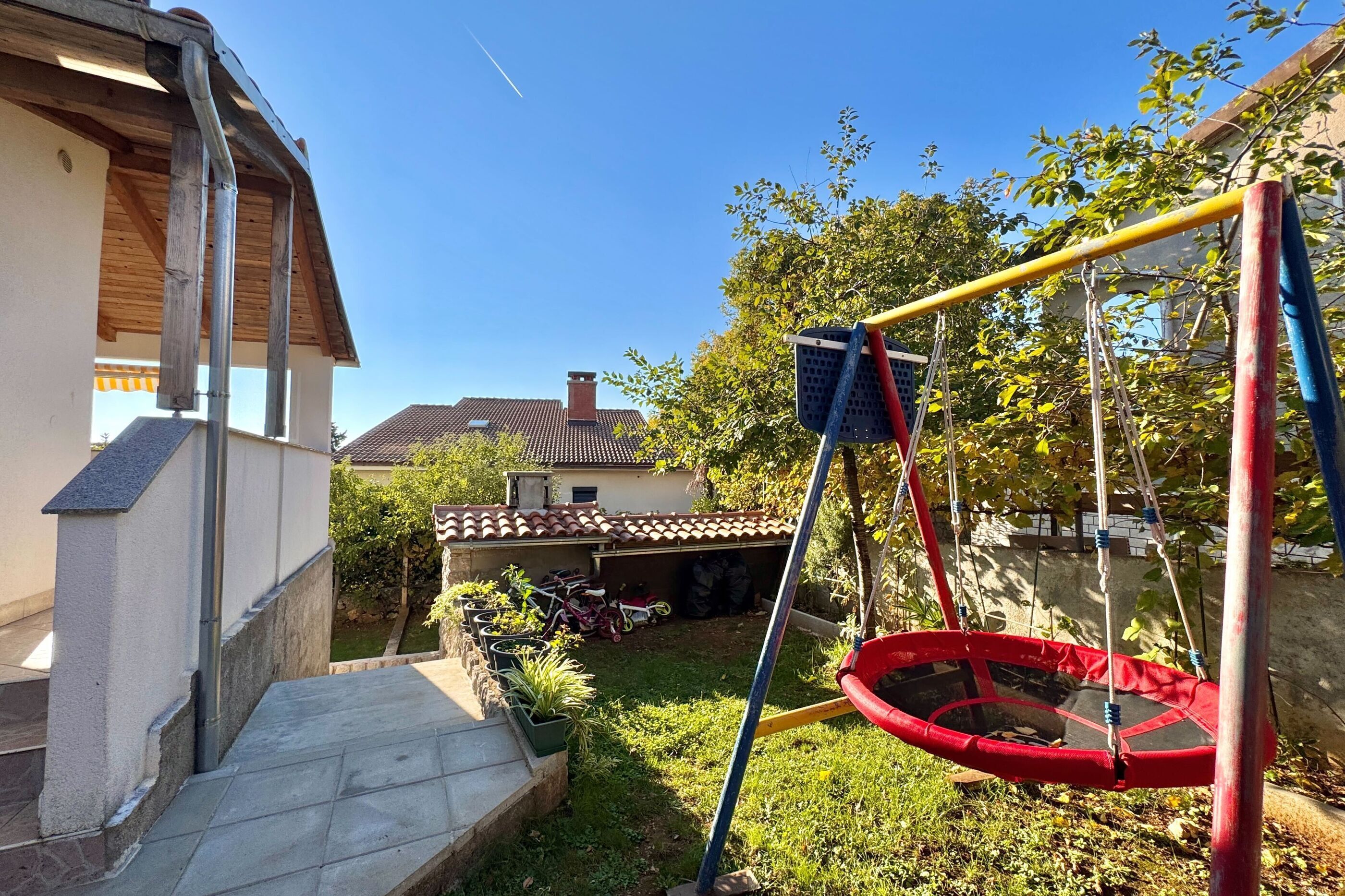 A residential backyard with a swing set, a trampoline, and a small garden area.