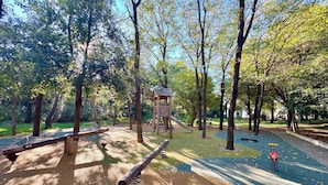 A playground with seesaws, a climbing structure, and a swing set in a wooded park area. - Apartments Matosic (Omisalj)