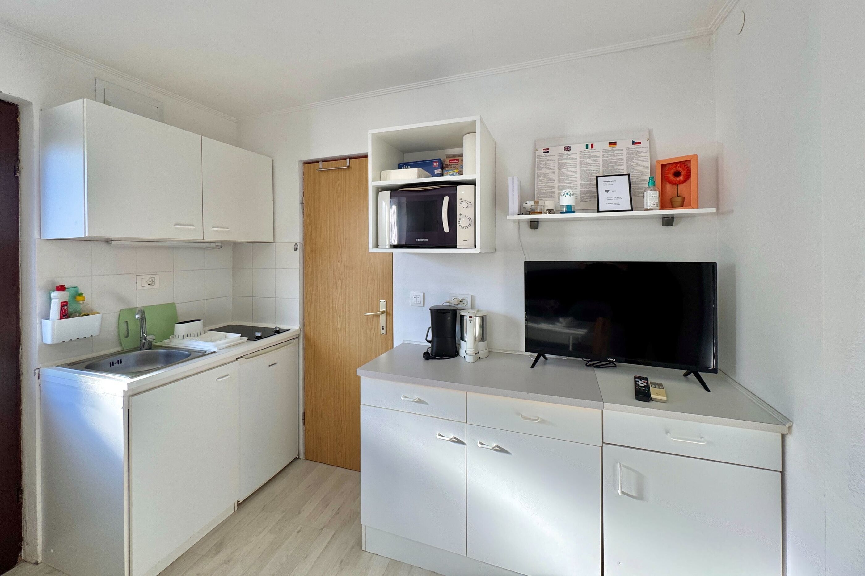A compact kitchen with white cabinets, a microwave, a coffee maker, and a TV.