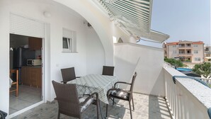 A balcony with a table and chairs, a kitchen area with a refrigerator and microwave, and a view of neighboring buildings. - Apartments Pejo (Vodice)
