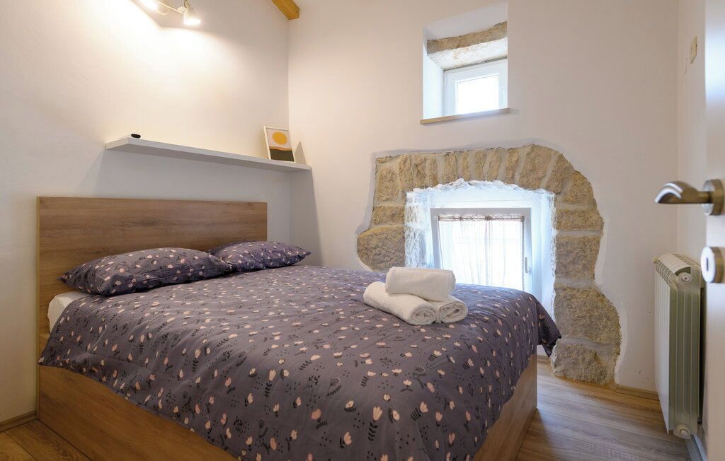 A bedroom with a bed, a stone wall, a window, and a radiator.