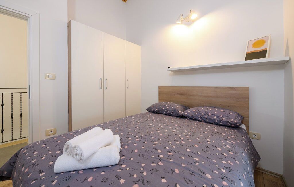 A bedroom with a bed, a wardrobe, a shelf with a picture, and a light fixture.