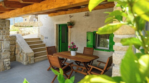 A stone staircase leading to a wooden deck with a table and chairs, green shutters, and a hanging plant. - House Casa Della Nonna (Krsan)