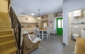 A modern kitchen with white cabinets, a dining area with a wooden table and white chairs, a staircase with a beige handrail, and a green door leading to a bathroom. - House Casa Della Nonna (Krsan)