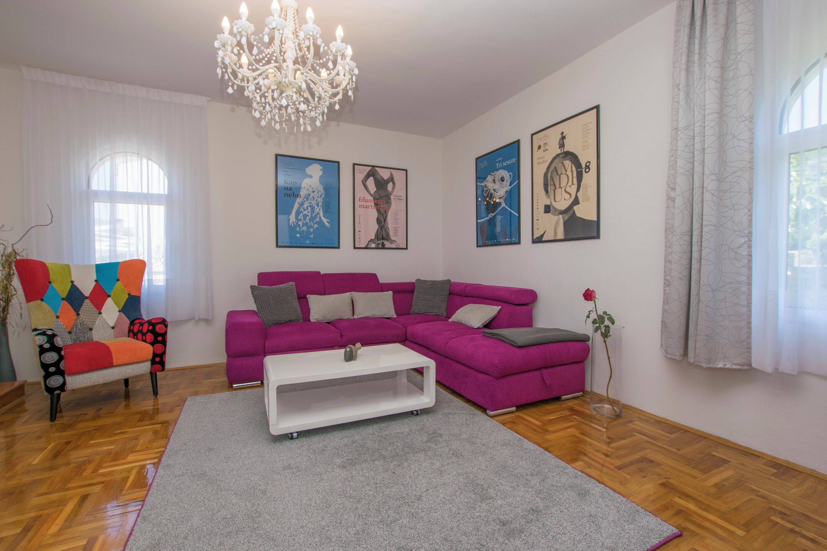Ein modernes Wohnzimmer mit einem violetten Ecksofa, einem weißen Couchtisch und bunten Stühlen.