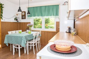 A dining area with a checkered tablecloth, white chairs, a window with a green valance, and a kitchen counter with various items. - House Zeleni Brig (Mrkopalj)