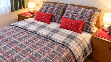 A neatly made bed with a plaid bedspread and two red pillows, flanked by nightstands with lamps and a small decorative item.