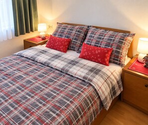 A neatly made bed with a plaid bedspread and two red pillows, flanked by nightstands with lamps and a small decorative item. - House Zeleni Brig (Mrkopalj)