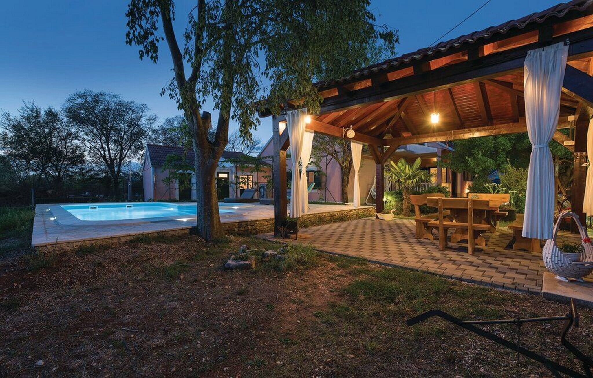 Un espace extérieur abrité comprenant une piscine, des meubles en bois et une pergola agrémentée de rideaux.