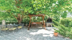 Une terrasse avec une balançoire en bois, un banc en pierre et une cheminée en briques.