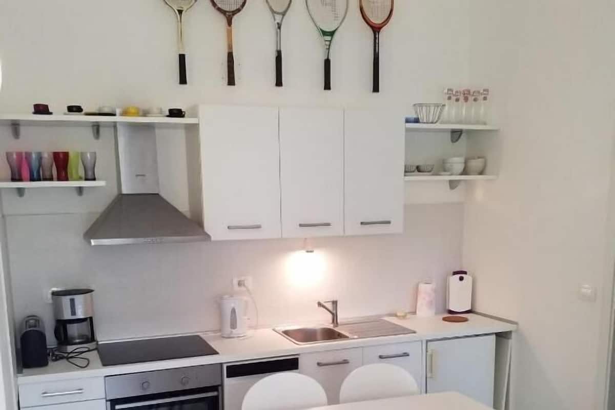 Una cocina compacta con armarios blancos, estufa, fregadero y una mesa de comedor con sillas.