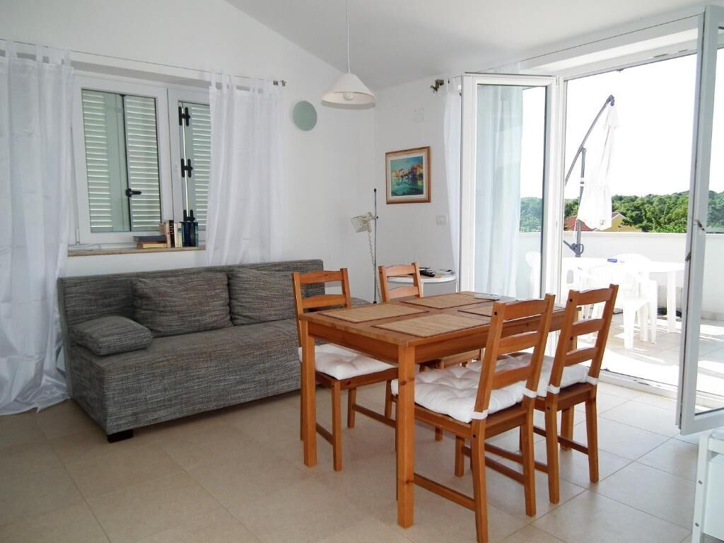 A room with a sofa, wooden dining table, chairs, a lamp, and a window with curtains.