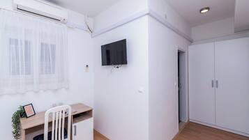Una habitación con escritorio de madera, una silla blanca, televisor montado y armario.