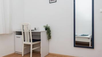 Uma mesa branca com uma cadeira, um pequeno vaso de plantas e um espelho refletindo uma cama.