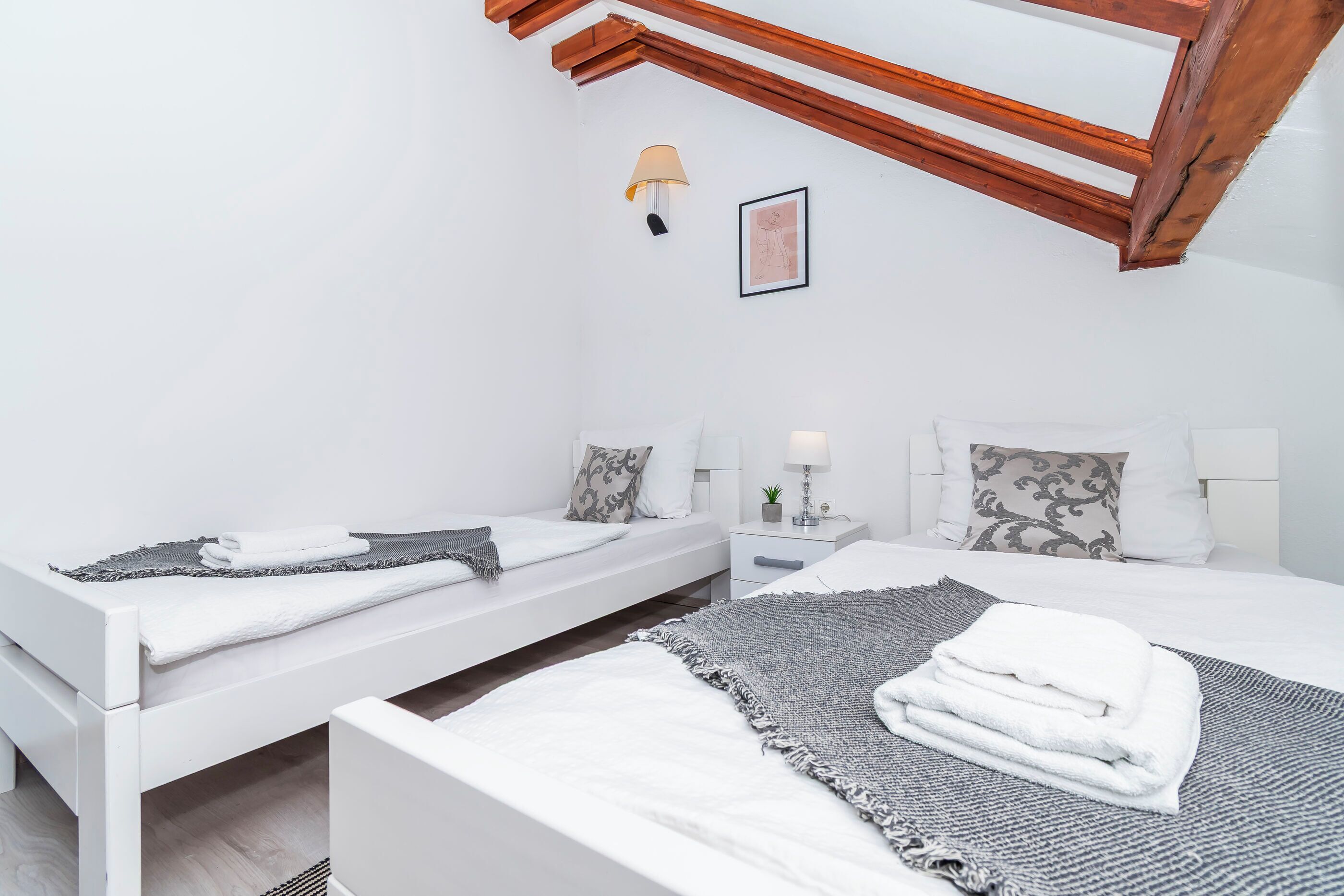 Ein modernes Schlafzimmer mit zwei Einzelbetten, einem Nachttisch mit Lampe und Deckenleuchte.