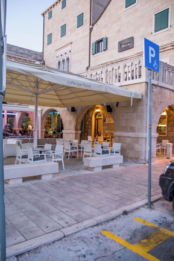 Un café bar con terraza, un letrero de estacionamiento y un edificio de piedra con ventanas de arco.