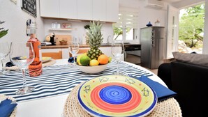 A dining table set with a colorful plate, a bowl of fruit, and wine glasses. - House Velebit by the sea (Senj)