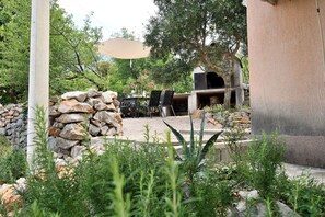 An outdoor patio with a stone wall, a grill, and a table with chairs. - House Velebit by the sea (Senj)